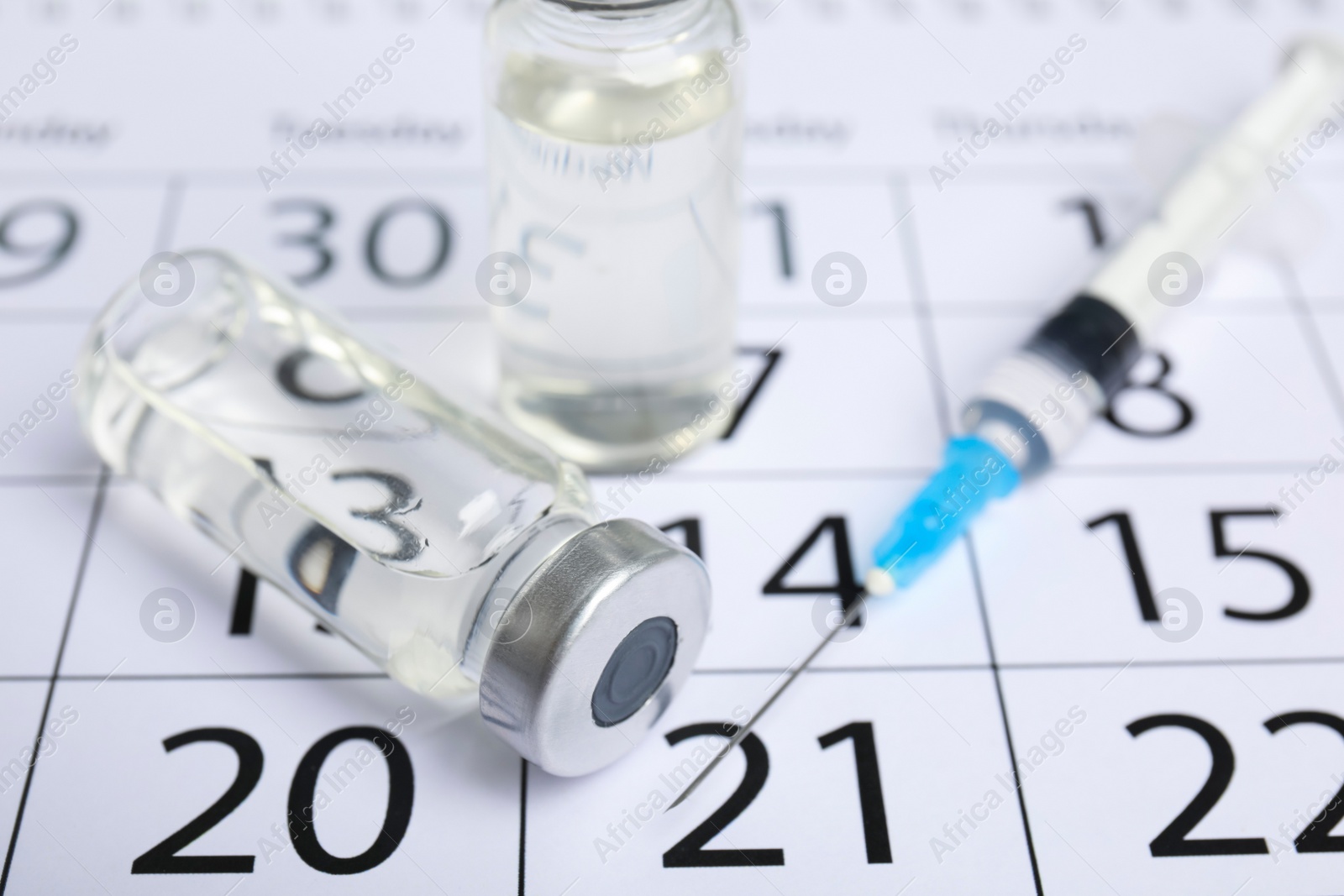 Photo of Vial and syringe on calendar, closeup. Vaccination and immunization