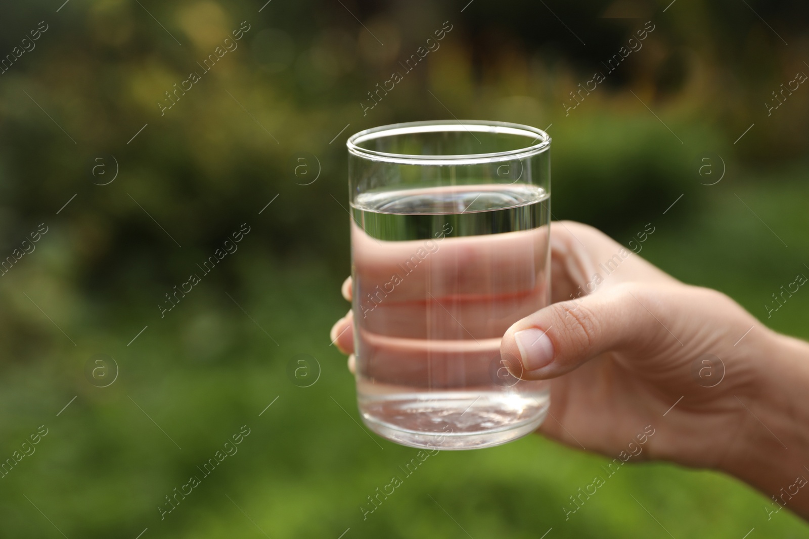 Photo of Woman holding glass of fresh water outdoors, closeup