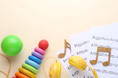 Photo of Wooden notes, music sheets, headphones and toys on beige background, flat lay with space for text. Baby song concept