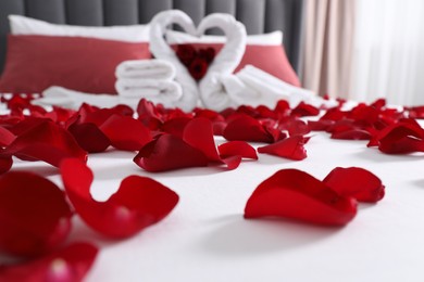 Photo of Honeymoon. Swans made with towels and beautiful rose petals on bed in room, selective focus