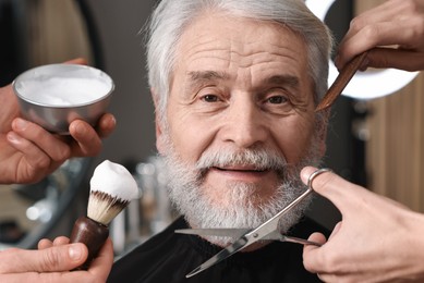 Photo of Professional barbers taking care of client's mustache and beard in barbershop