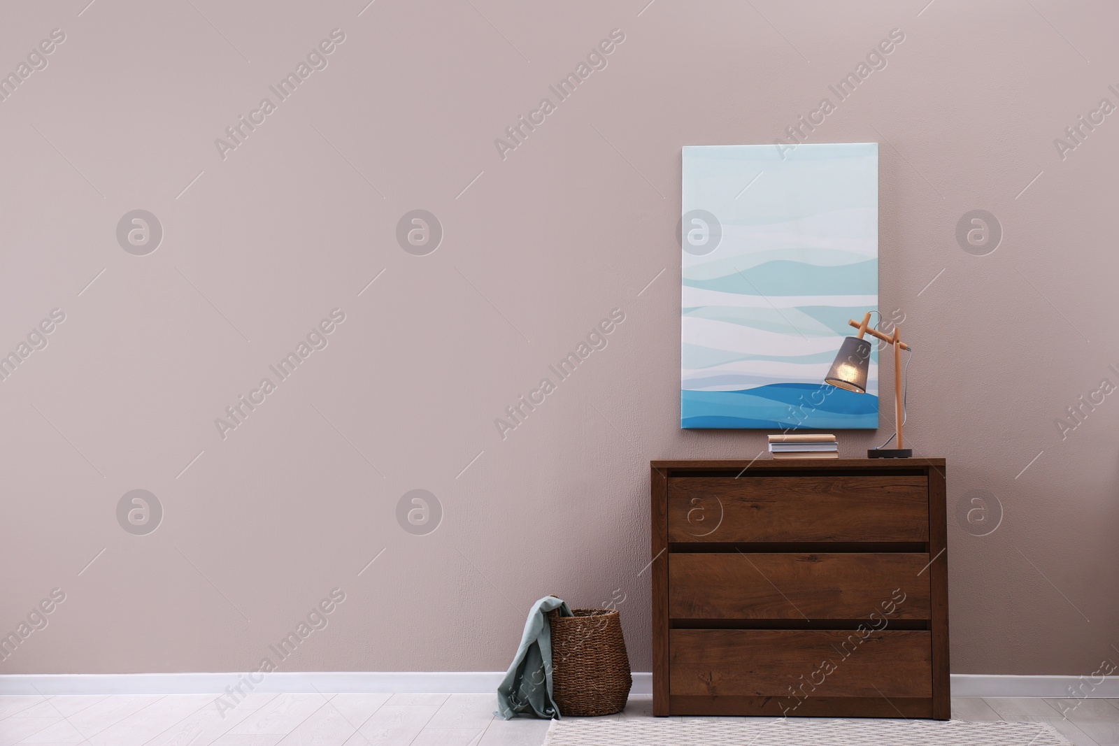 Photo of Wooden chest of drawers with books and lamp near beige wall in room, space for text. Interior design