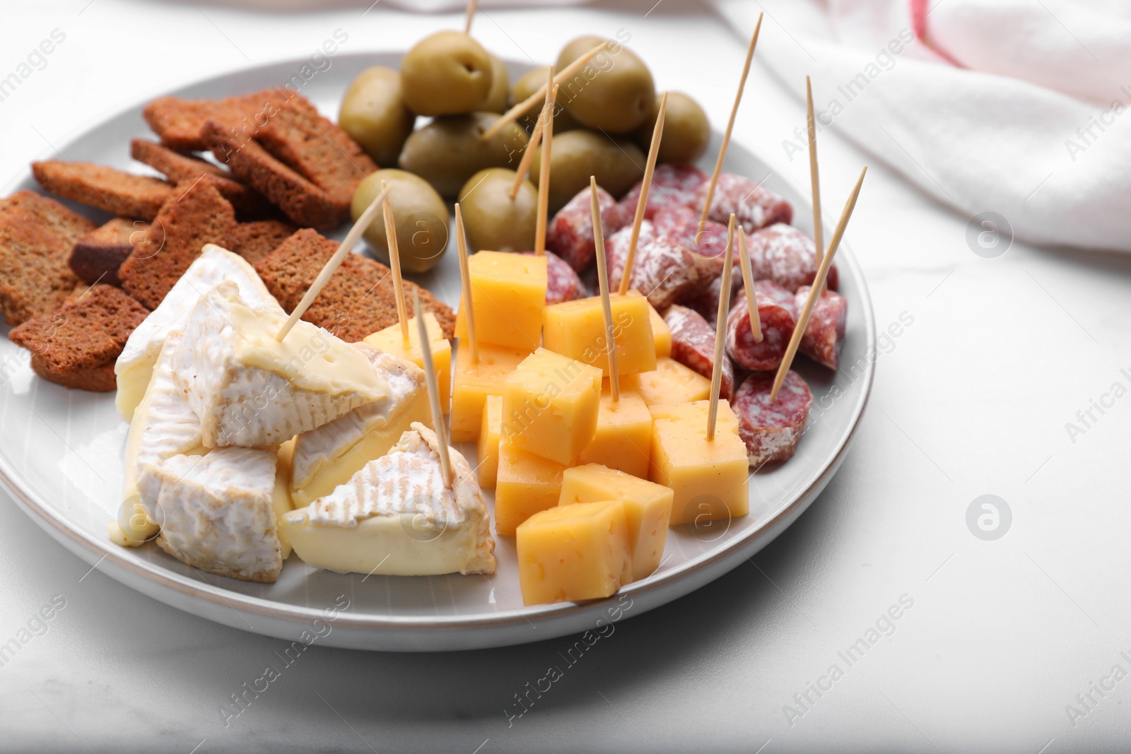 Photo of Toothpick appetizers. Pieces of different cheese, sausage and olives on white table