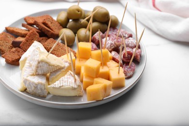 Photo of Toothpick appetizers. Pieces of different cheese, sausage and olives on white table