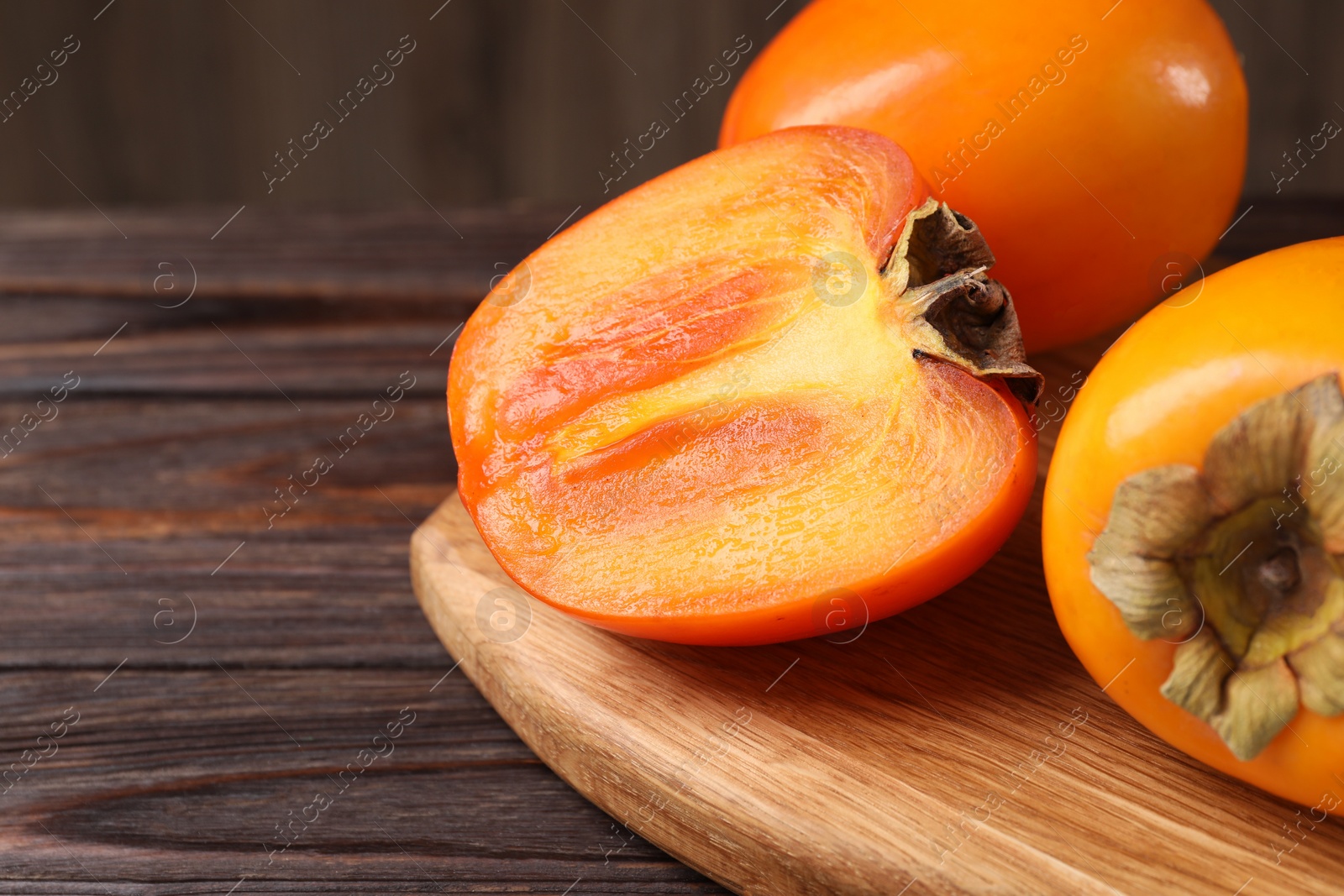 Photo of Whole and cut delicious ripe persimmons on wooden table, closeup. Space for text