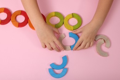 Photo of Motor skills development. Girl playing with colorful wooden arcs at pink table, top view
