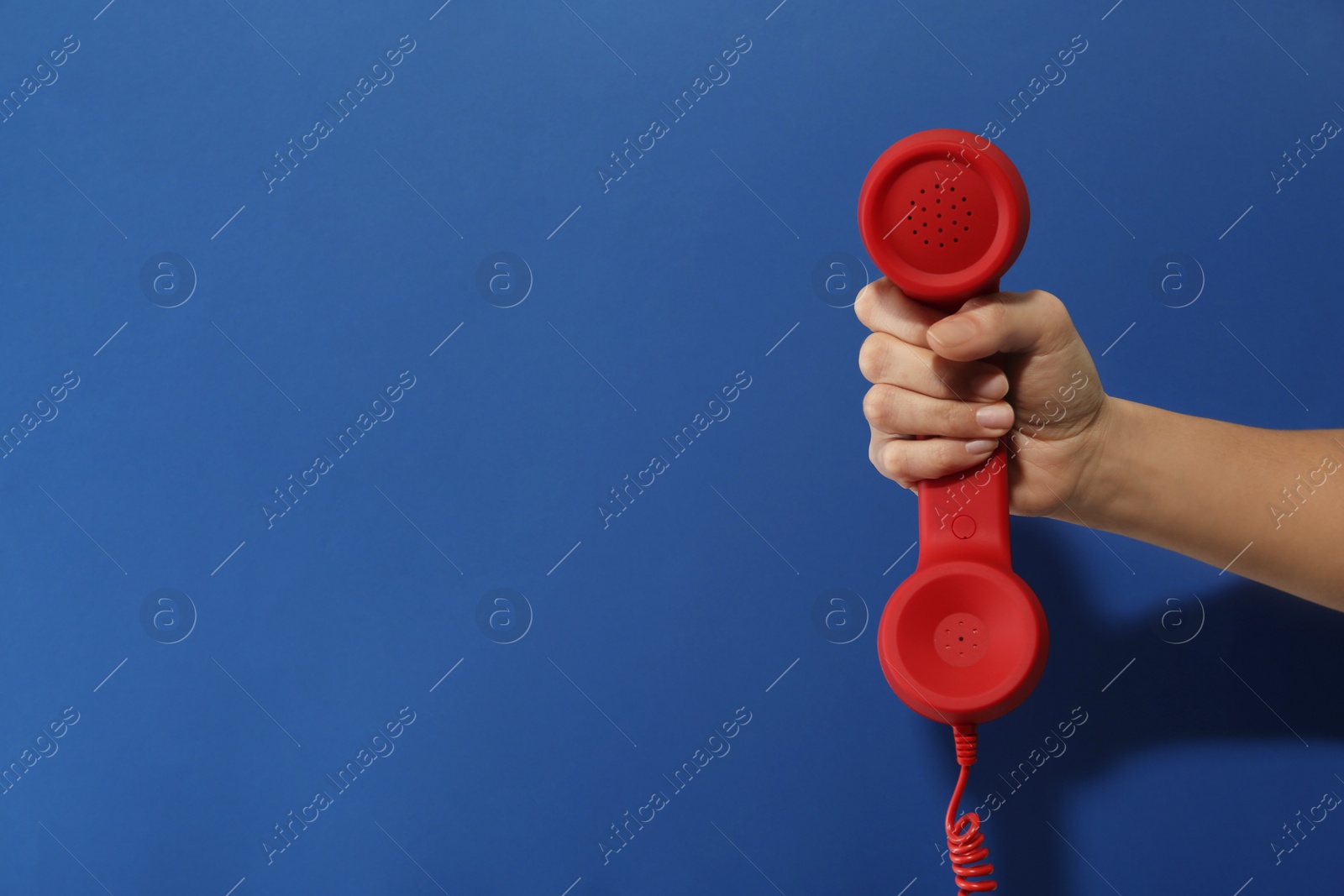 Photo of Closeup view of woman holding red corded telephone handset on blue background, space for text. Hotline concept