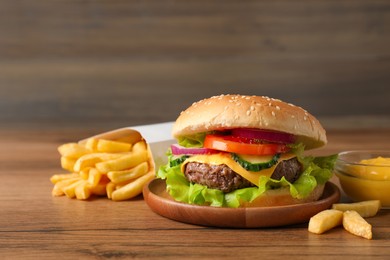 Photo of Delicious burger, sauce and french fries served on wooden table