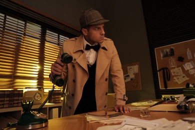 Photo of Old fashioned detective picking up phone in office