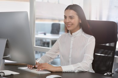 Photo of Happy woman using modern computer at black desk in office