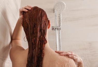 Photo of Young woman washing her hair with shampoo in shower, back view