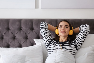 Photo of Young woman with headphones enjoying music in bed