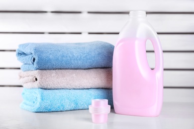 Photo of Laundry detergent and clean towels on table against blurred background