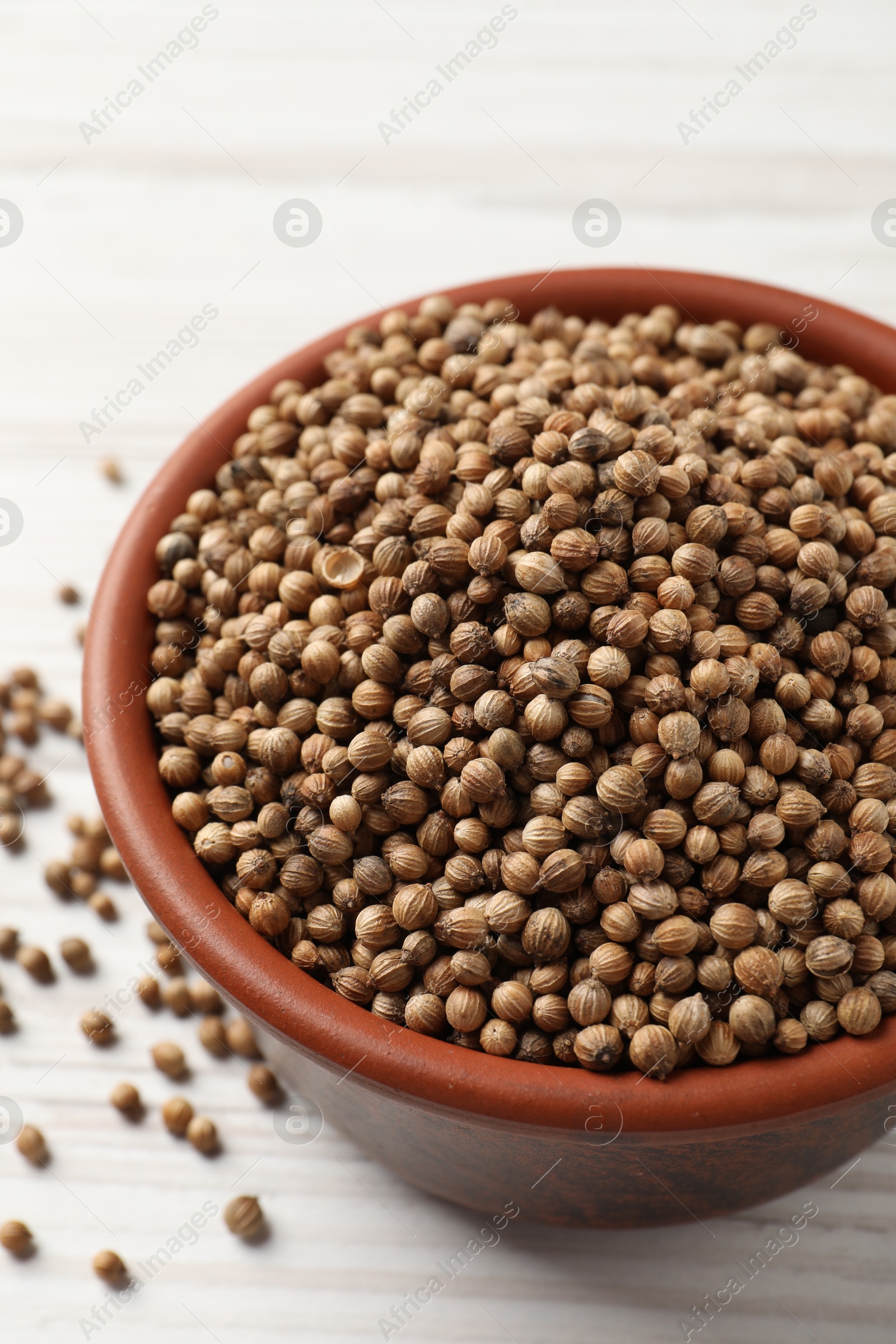 Photo of Dried coriander seeds in bowl on wooden table, closeup