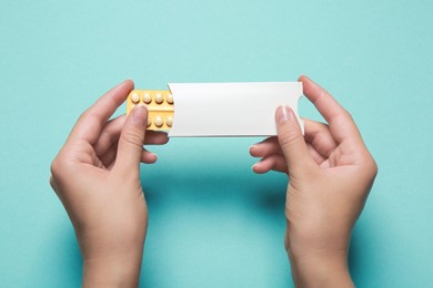 Photo of Woman holding birth control pills on light blue background, top view