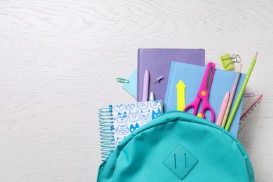 Photo of Schoolbag with books and stationery on wooden table, flat lay. Space for text