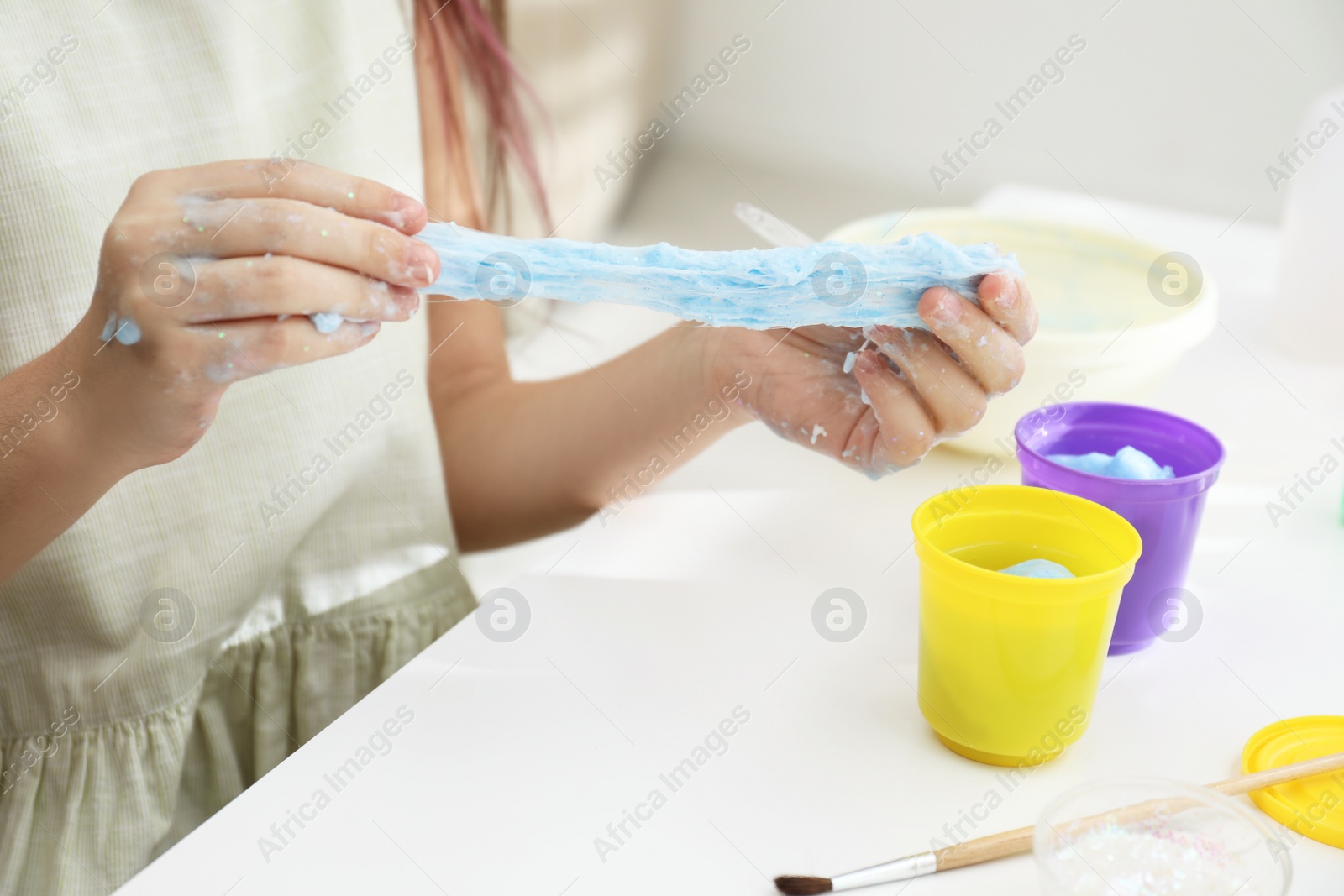 Photo of Little girl making DIY slime toy at table, closeup