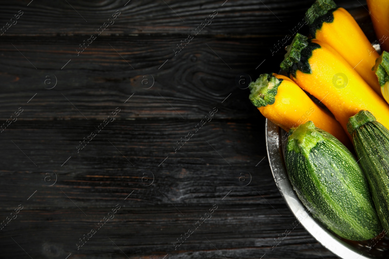 Photo of Colander with fresh ripe zucchini on black wooden background, top view. Space for text