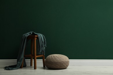 Stylish knitted pouf and wooden stool with blanket near green wall indoors, space for text
