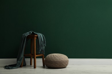 Photo of Stylish knitted pouf and wooden stool with blanket near green wall indoors, space for text