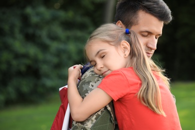 Father in military uniform with American flag hugging his little daughter at green park
