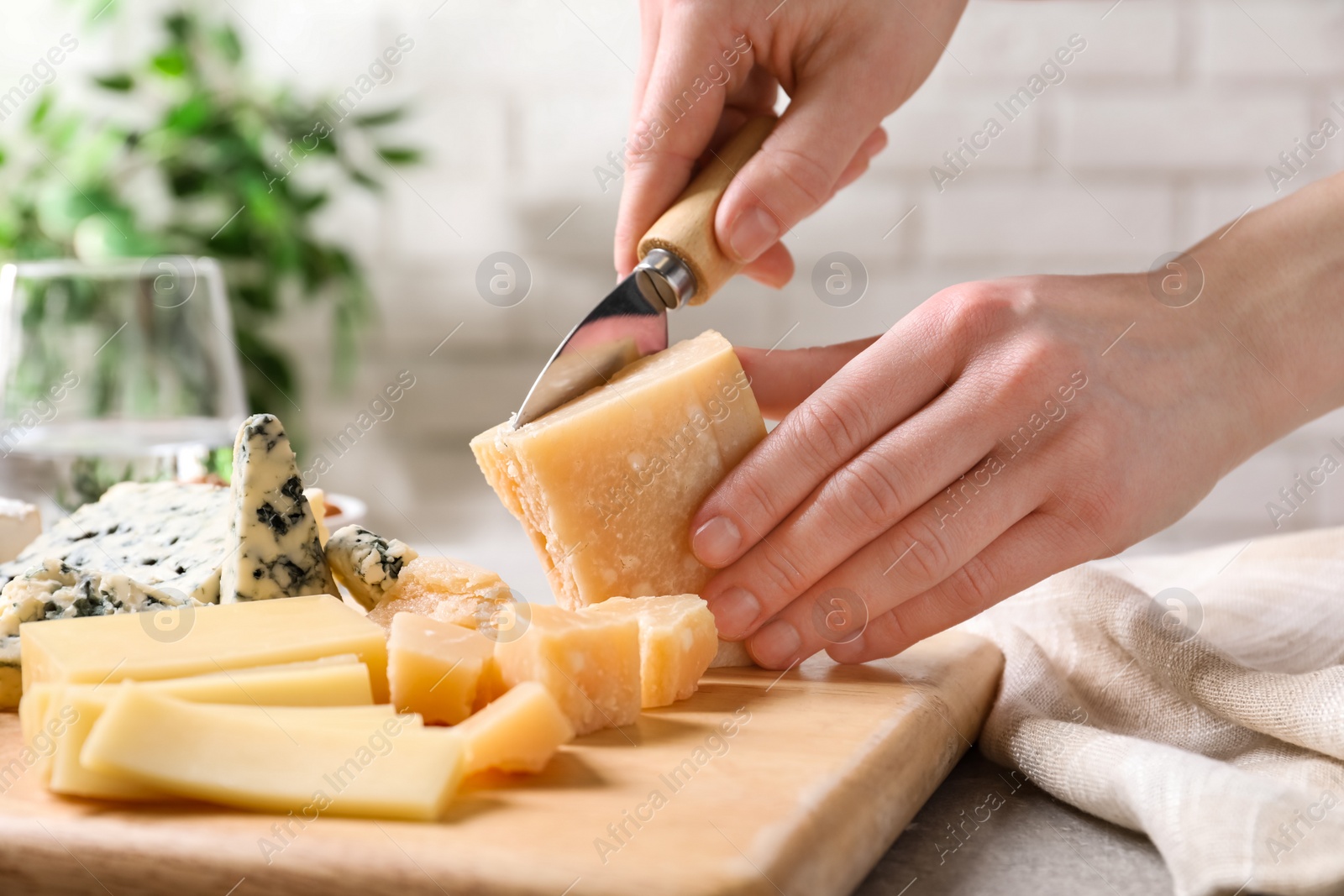 Photo of Woman cutting parmesan for cheese plate at table, closeup