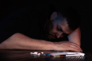 Overdosed man at table, focus on different drugs