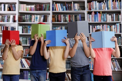 Photo of Group of little children holding books near shelves in library reading room