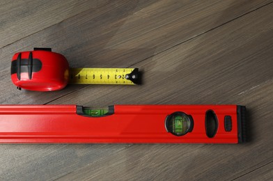 Building level and tape measure on wooden table, top view