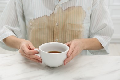 Photo of Woman with spilled coffee over her shirt sitting at marble table, closeup