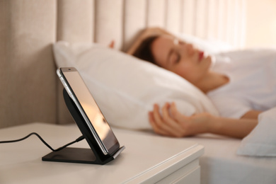 Smartphone charging on wireless pad and woman sleeping in bed