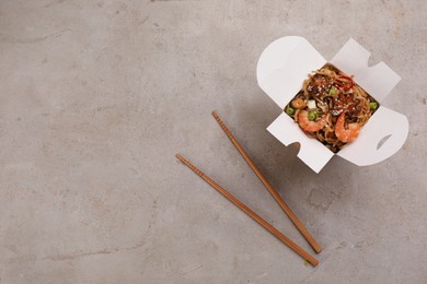 Box of wok noodles with seafood and chopsticks on light table, flat lay. Space for text