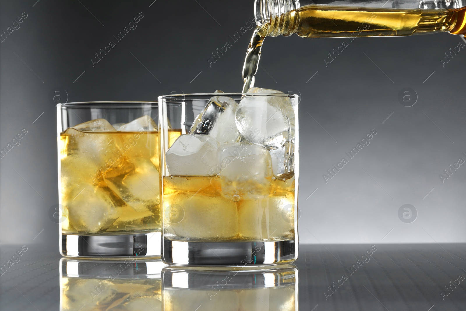 Photo of Pouring tasty whiskey from bottle into glass at mirror table, closeup