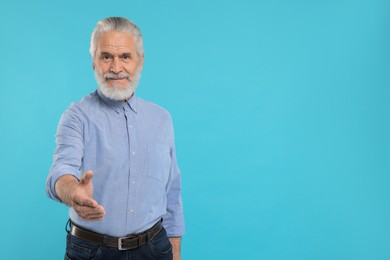 Photo of Senior man welcoming and offering handshake on light blue background, space for text
