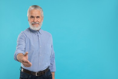 Senior man welcoming and offering handshake on light blue background, space for text