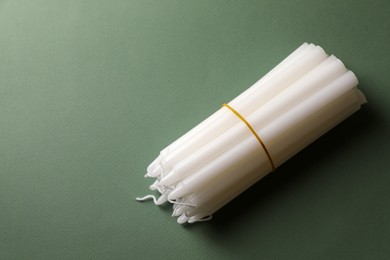 Many church wax candles on olive background, above view. Space for text