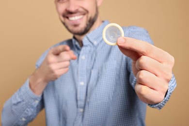 Happy man holding condom on beige background, closeup