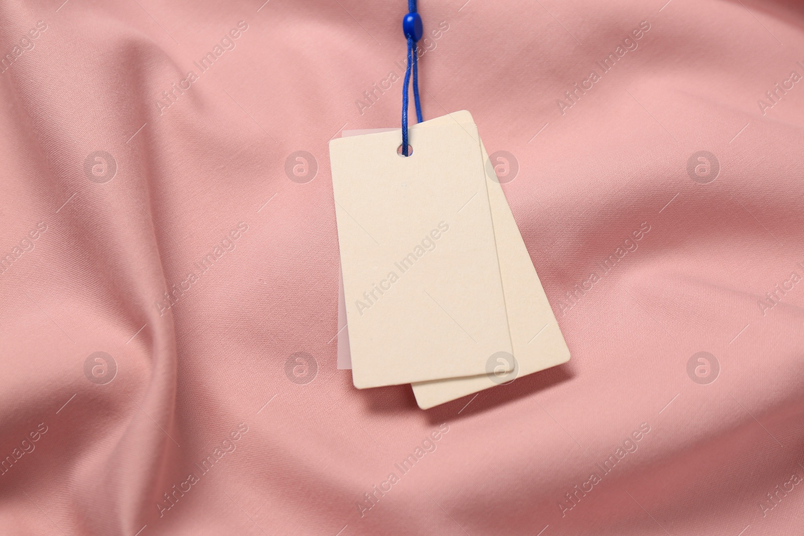 Photo of Blank white tags on pink fabric. Space for text