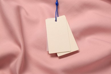 Photo of Blank white tags on pink fabric. Space for text