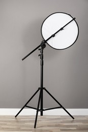 Photo of Professional light reflector on tripod near grey wall in room. Photography equipment
