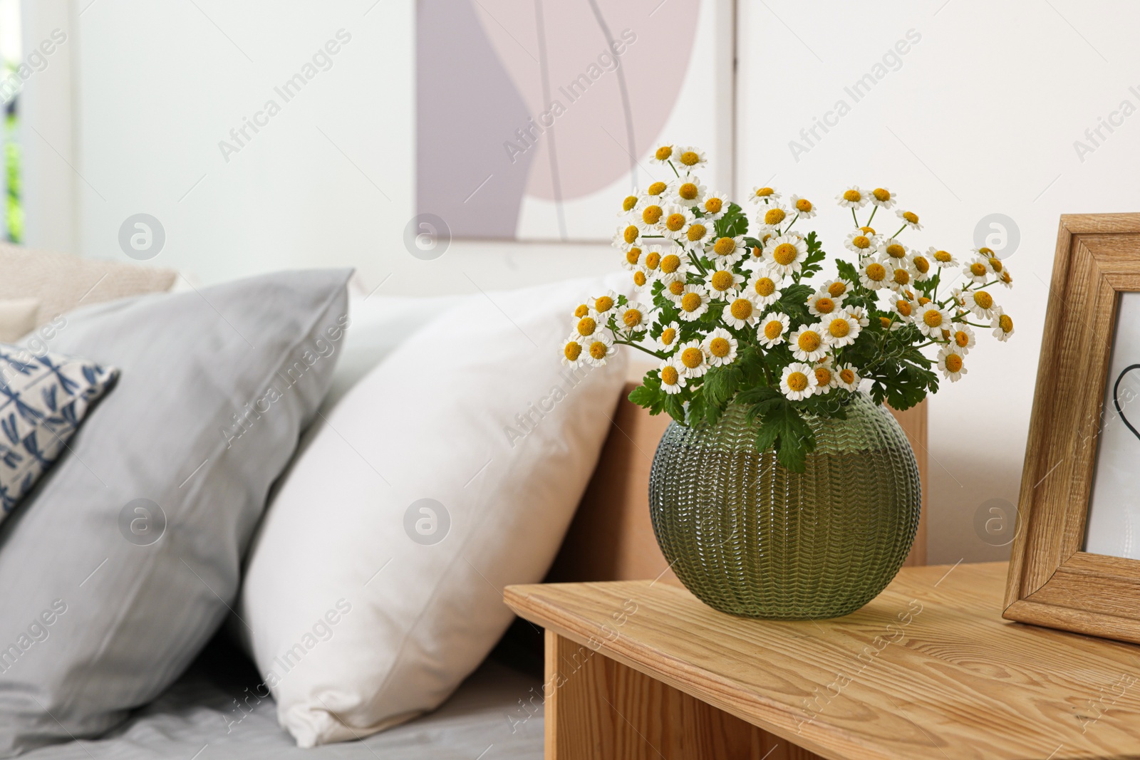 Photo of Beautiful bouquet of chamomile flowers on wooden nightstand in bedroom, space for text. Interior element