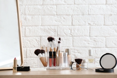 Organizer with cosmetic products for makeup on table near brick wall