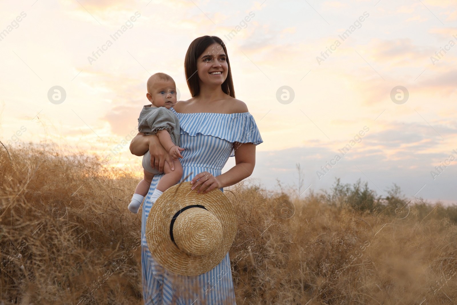 Photo of Happy mother with adorable baby in field at sunset