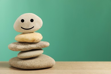 Photo of Closeup view of stones with drawn happy face on table against turquoise background, space for text. Zen concept