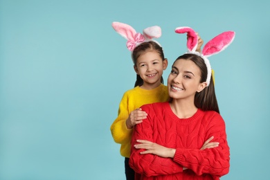 Photo of Mother and daughter in Easter bunny ears headbands on color background, space for text