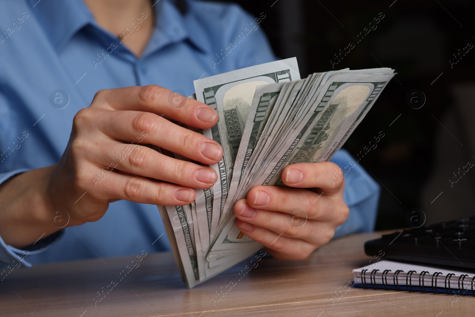 Photo of Money exchange. Woman counting dollar banknotes at wooden table, closeup