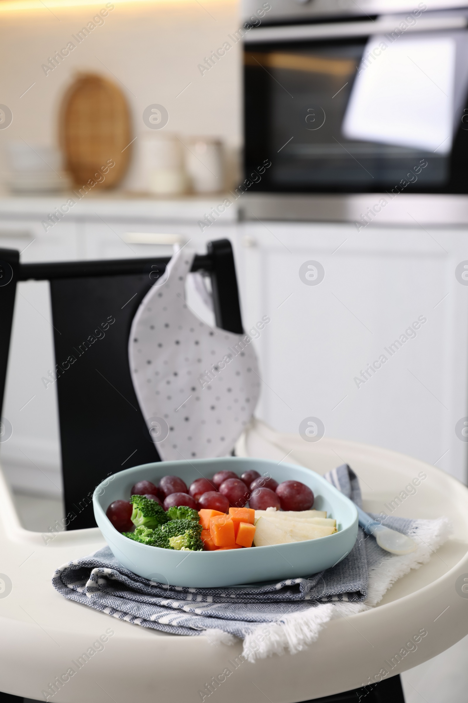 Photo of High chair with food in baby tableware on tray indoors