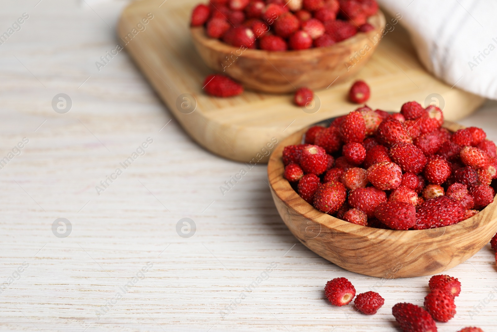 Photo of Fresh wild strawberries in bowls on white wooden table. Space for text