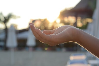 Photo of Girl holding her hand against sunlight on beach, closeup