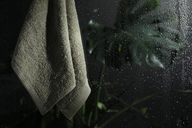 Terry towel hanging on wet glass wall in shower, space for text